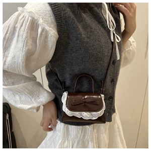 Detail of dark brown patent leather mini bag with lace trim and sweet bow decoration