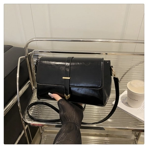 Detailed view of black patent leather bag with a gold heart clasp and strap decoration
