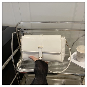 Detailed shot of white leather crossbody bag with gold metal buckle on a stylish shelf