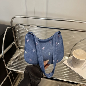 Blue denim crescent bag with white and pink bow patterns shown in a hand-held display