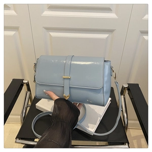 Detail of light blue crossbody bag featuring a gold heart-shaped metal buckle and strap