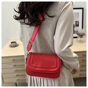 Detail of red faux suede saddle bag featuring quilted lines and adjustable wide strap