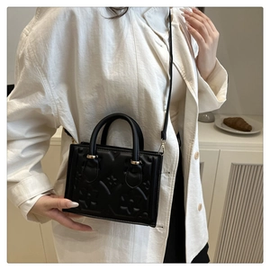 Detail of black embossed handbag featuring floral texture and golden metal hardware