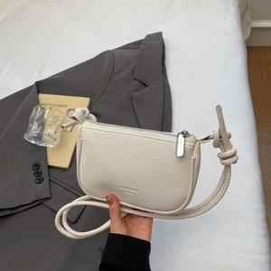 Minimalist beige pebble leather crescent shoulder bag with knotted strap and zip closure