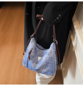 Detail of light blue denim tote bag featuring silver metal logo and brown leather strap
