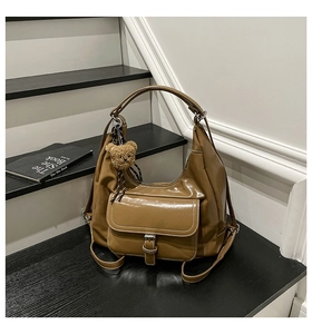 Detail of a brown glossy leather hobo bag with a front buckle pocket and bear charm
