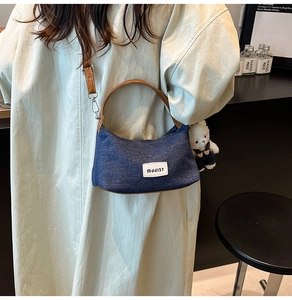 Close-up of denim hobo bag featuring brown leather straps and a white plush bear charm
