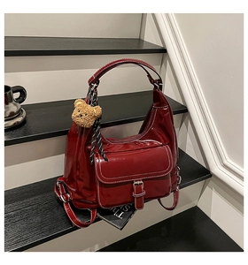 Detail of dark red patent leather shoulder bag with plush bear charm and white topstitching