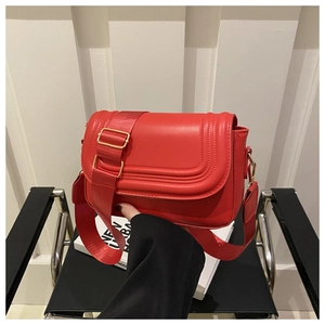 Detail of red leather saddle bag with wide strap and golden hardware accents