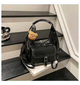 Detail of black hobo bag with white stitching, leather buckle pocket and bear charm