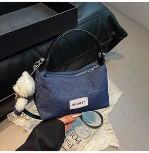 Détail du sac à main en denim avec poignée en cuir, patch logo et charm ours peluche