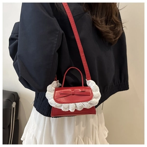 Red leather crossbody bag with white lace embroidery and bow detail on model