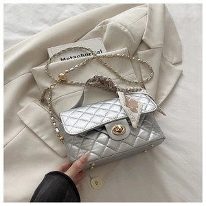Detail of silver quilted handbag with golden chain strap and silk scarf handle decor