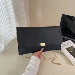 Minimalist black Saffiano envelope bag with gold chain strap in a lifestyle setting