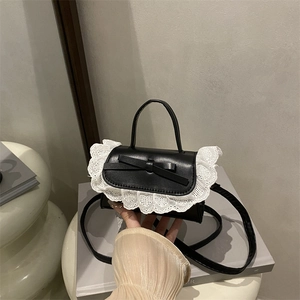 Chic black balletcore crossbody bag with white lace trim and bow on a book base