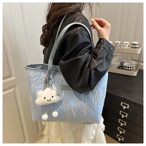 Detail of light blue quilted tote bag with colorful wave embroidery and cloud charm