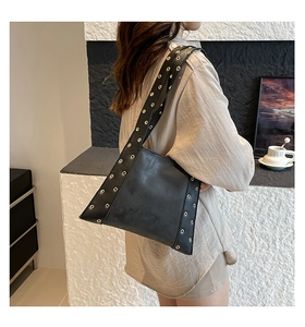 Détail du sac bandoulière en cuir mat noir avec des rivets oeillets dorés sur la sangle