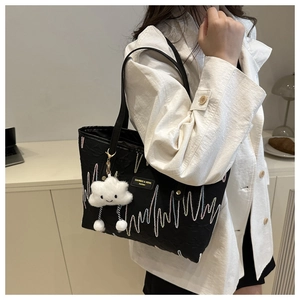 Detail of black tote bag featuring wavy embroidery and a plush cloud charm accessory