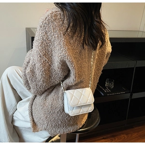 Détail d'un sac à bandoulière en cuir blanc matelassé avec chaîne sur gilet kaki