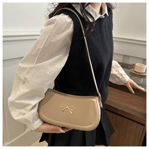 Detail of milk tea leather underarm bag featuring a golden bow metal ornament