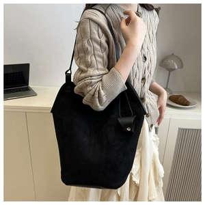 Side view of a black suede tote bag with triangle pendant on a casual model in a room