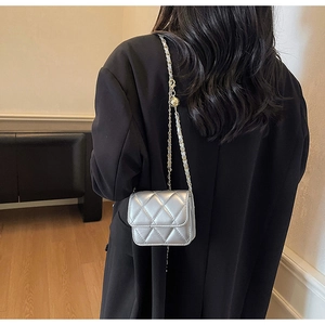 Détail du sac argenté matelassé avec chaîne dorée ajustable sur un blazer noir