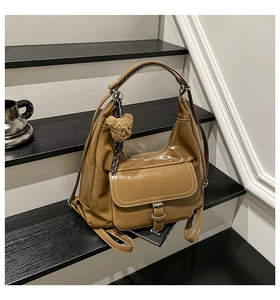 Detail of camel brown crossbody bag featuring white stitching and a plush bear charm