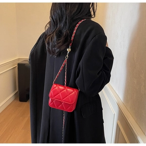 Détail du mini sac bandoulière matelassé rouge avec chaîne dorée sur manteau noir