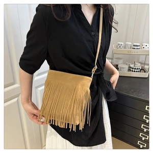 Detail view of camel suede fringe bag with bohemian tassels worn by a model