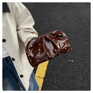 Détail d'une pochette marron foncé plissée avec des clous et finition brillante