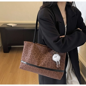Detail of leopard print tote bag with fuzzy monster charm on a stylish shoulder strap