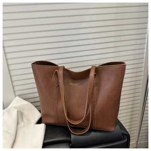 Detail of a brown leather tote bag showing a gold logo print and fine pebbled texture