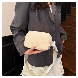 Beige nylon crossbody fanny pack shown with adjustable woven strap and plastic buckle