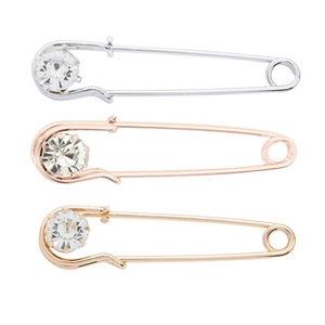 Close-up of three decorative safety pins with rhinestones in silver, gold, and rose gold