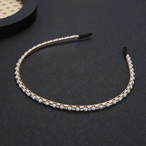 Golden metal headband with pearls and rhinestones on a textured black surface