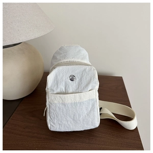 Detail of white wrinkled nylon chest bag with round metal logo on a wooden desk