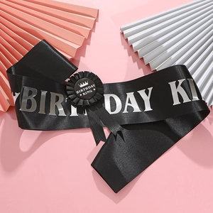 Détail de l'écharpe Birthday KING en satin noir avec texte argenté et son badge