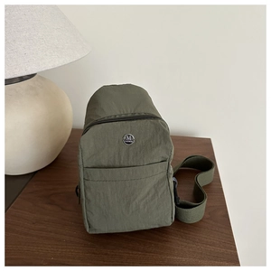 Close-up of army green nylon chest bag with metal logo on textured wooden table