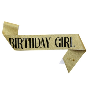 Close-up of golden glitter Birthday Girl sash with bold black text and safety pin