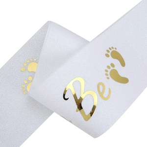 Close-up of white glitter sash with gold foil Mommy to Be text and baby footprints