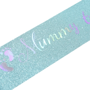 Macro detail of light blue glitter sash with holographic Mummy to Be lettering and footprints