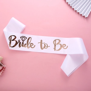 Close-up of white satin Bride to Be sash with rose gold lettering and diamond pattern