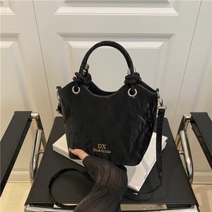 Chic black pleated leather bucket bag with top handle and gold branding on a modern chair