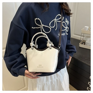 Detail of white bucket bag with brown trim and adjustable strap worn by model