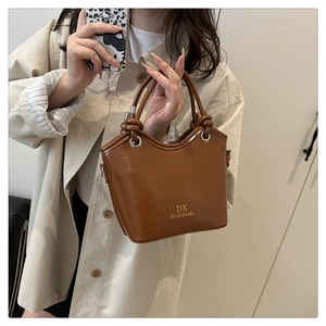 Close-up of brown leather bucket bag showing knotted handle and gold logo detail