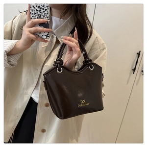 Detail of glossy coffee bucket bag showing smooth patent leather finish and golden logo