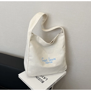 Detail of white canvas hobo bag with blue C'est la vie text on a minimalist background