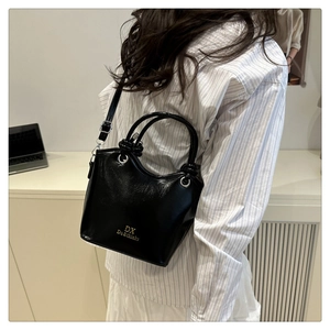 Glossy black bucket bag with gold logo shown on model for a casual styling reference
