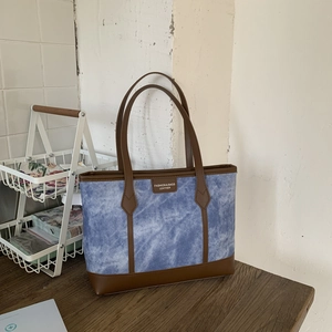 Chic blue denim tote bag with brown leather trim for commuting, shown on wooden table