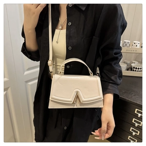 Close-up of cream white glossy leather handbag featuring elegant gold V-shaped metal buckle